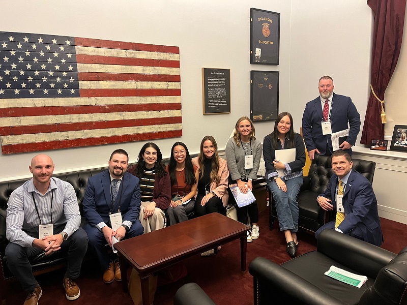 People seated and smiling in an office with an American flag wall art behind them.