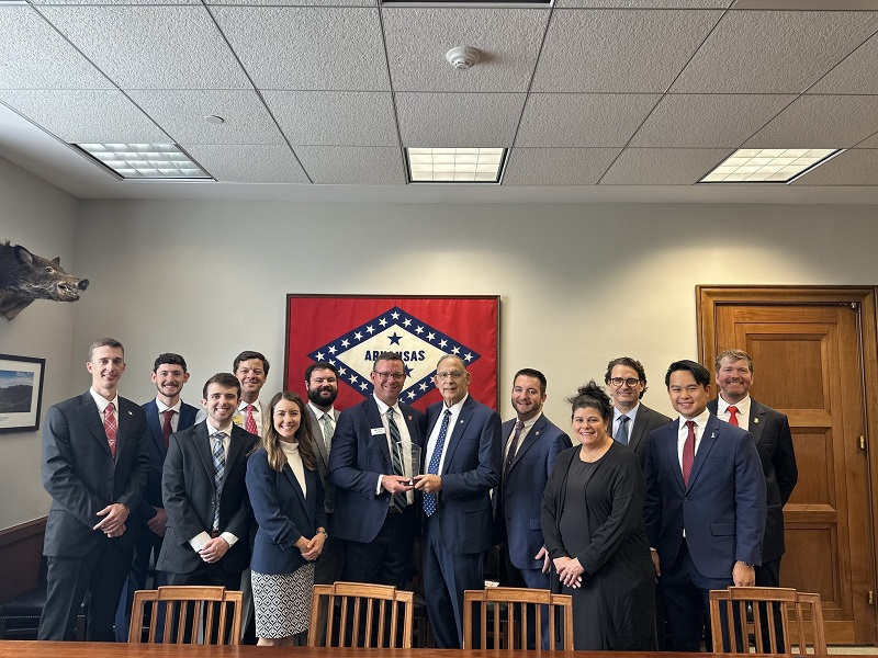 Group of NSUOCO students posing in an office with the Arkansas state flag on the wall.